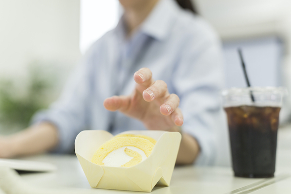 京橋 銀座みらい歯科＿仕事をしながらロールケーキに手を伸ばして食べようとする女性のイメージ